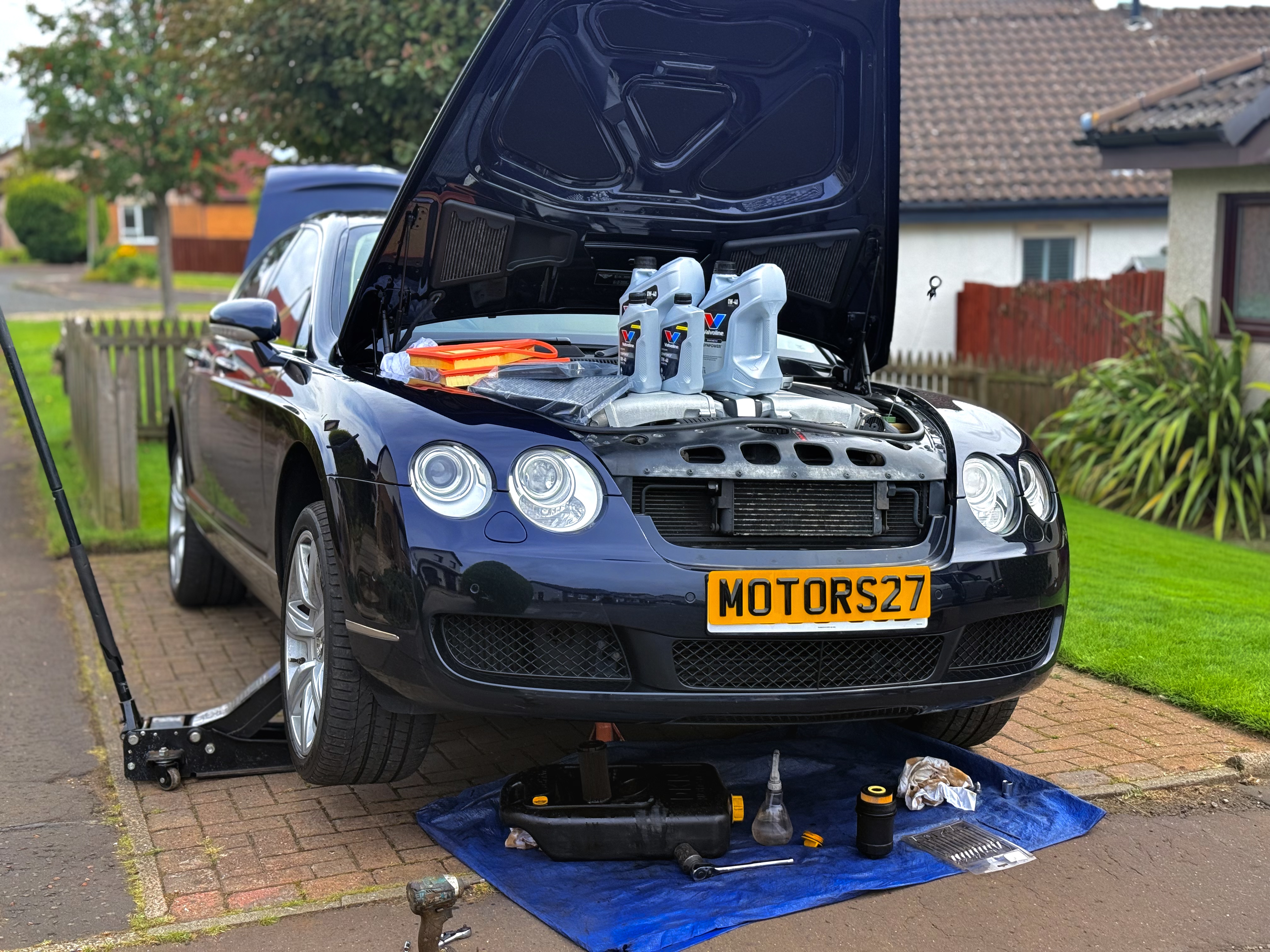 Vehicle servicing with engine oil, filters and tools beside a Bentley
